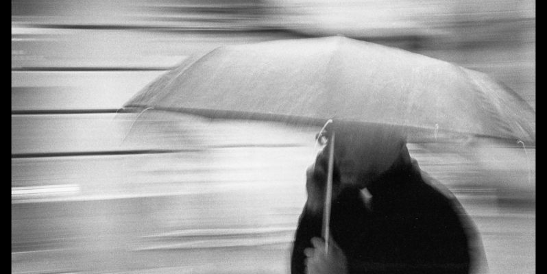 Motion-Blurred Image of a Priest in the Rain under an umbrella