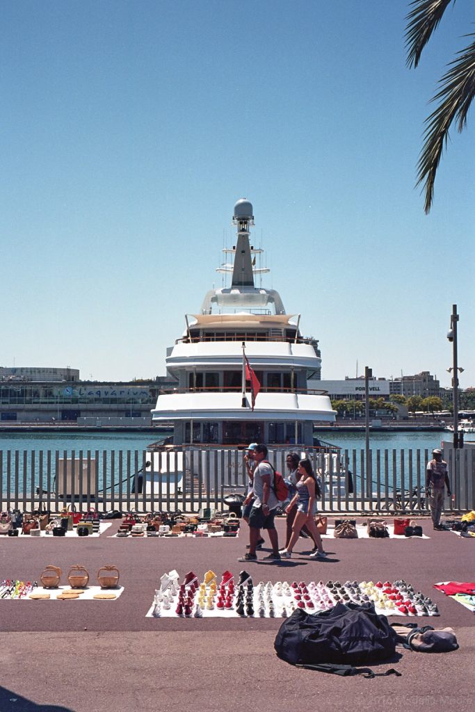 Illegal street-sellers in front of a luxury yacht, Barceloneta.